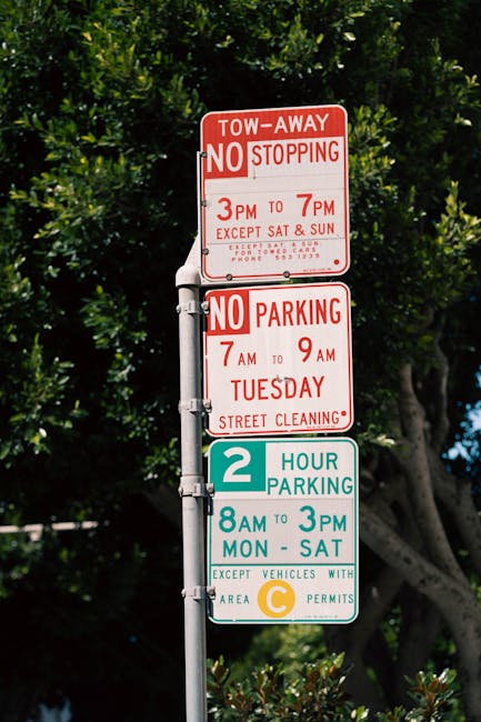 A weathered metal sign attached to a pole indicating that the space is reserved 24 hours, with peeling paint and rust visible on the sign and pole. The background features a white wall with signs of d