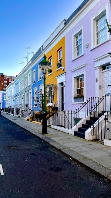 A residential street in Kensington lined with parked cars on both sides, with well-maintained white and beige terraced houses featuring large windows and decorative moldings. The street is framed by b
